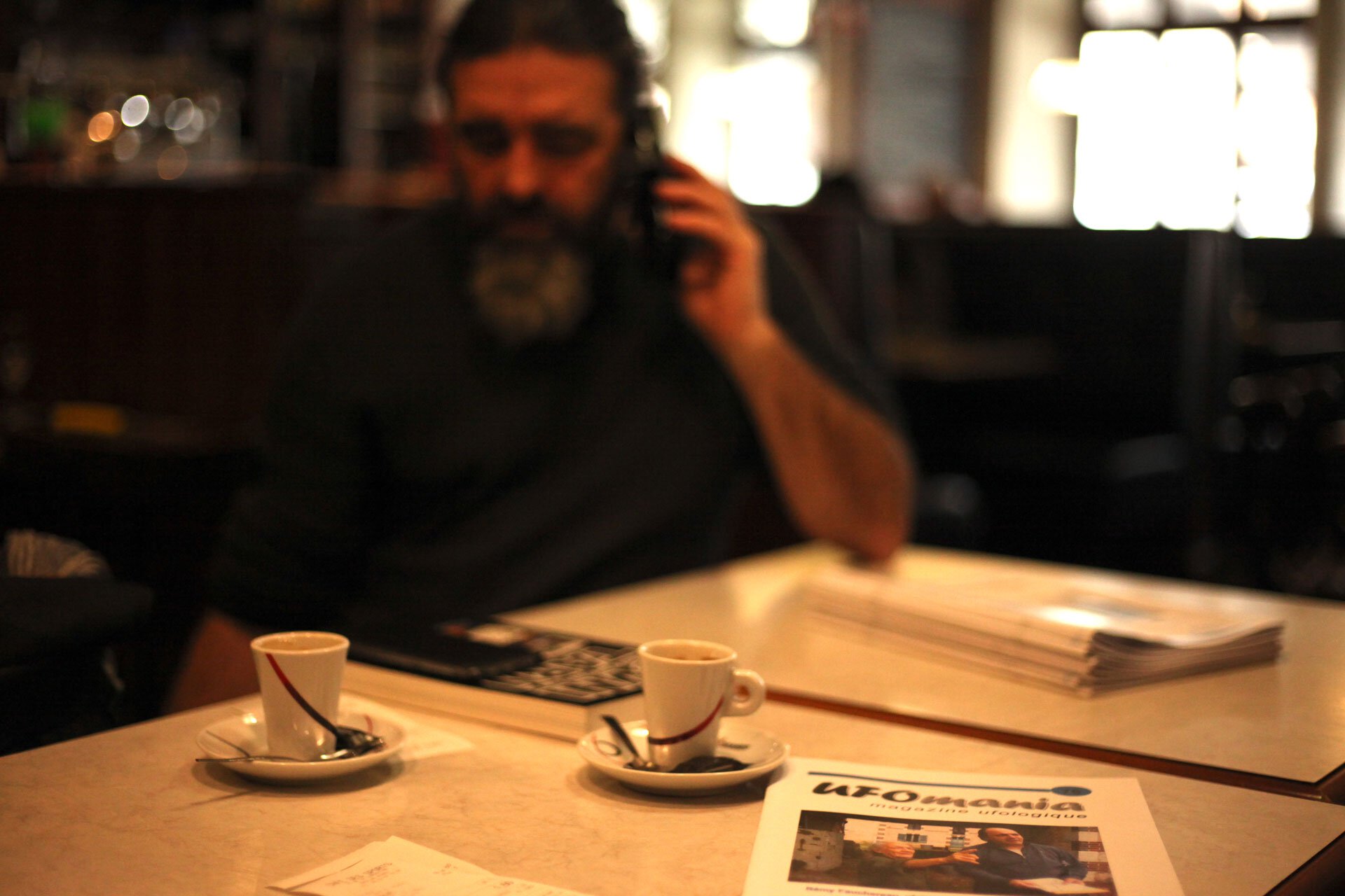 Didier Gomez au téléphone devant son café et le magazine UFO Mania.