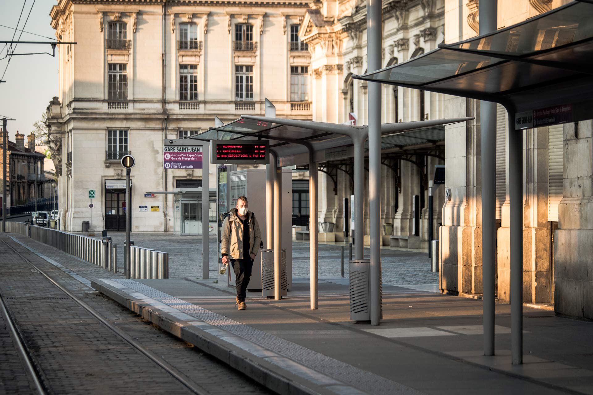 Un homme, seul, erre devant la Gare Saint-Jean à la tombée du soleil. 